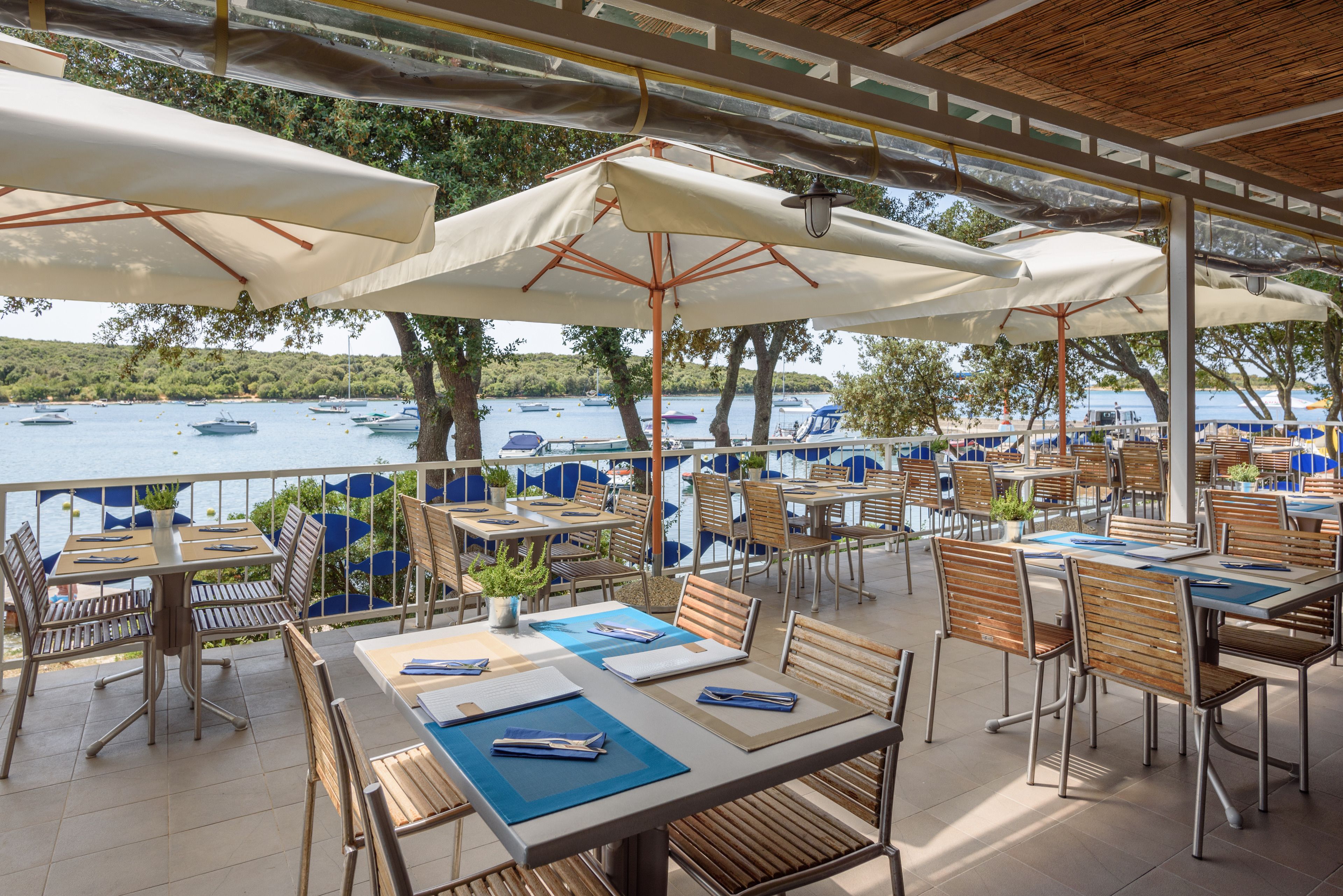 A terrace with tables and chairs, overlooking a body of water with boats.