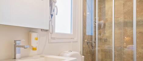A modern bathroom with a white vanity, a toilet, a glass-enclosed shower, and a window providing natural light.