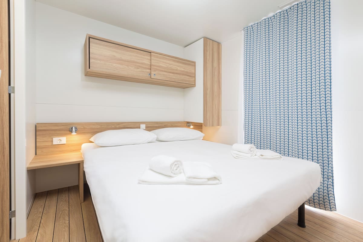 A hotel room with a wooden headboard, a bed with white linens, a nightstand, and a wall-mounted cabinet.