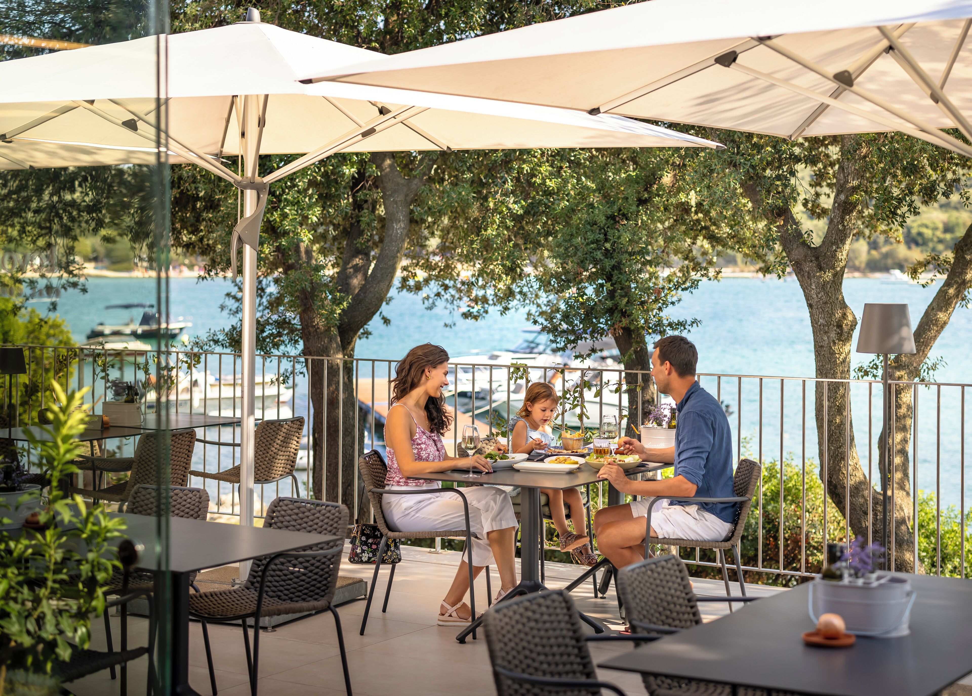 An outdoor dining area with tables and chairs, umbrellas, and a view of the sea.