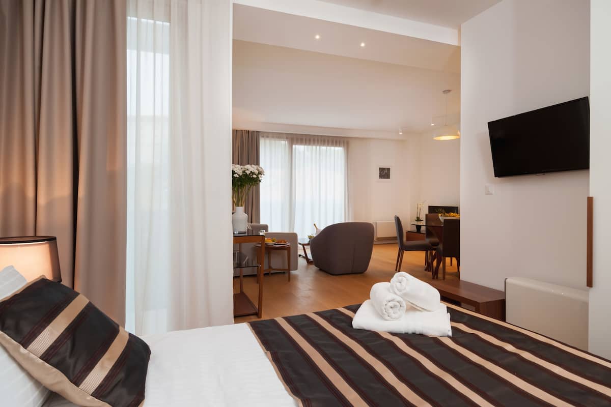 A hotel room with a bed, a desk, a chair, a TV, and a view of the dining area.