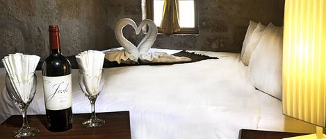 Quarto de hotel com uma cama, uma garrafa de vinho e duas taças de vinho sobre uma mesa de madeira.