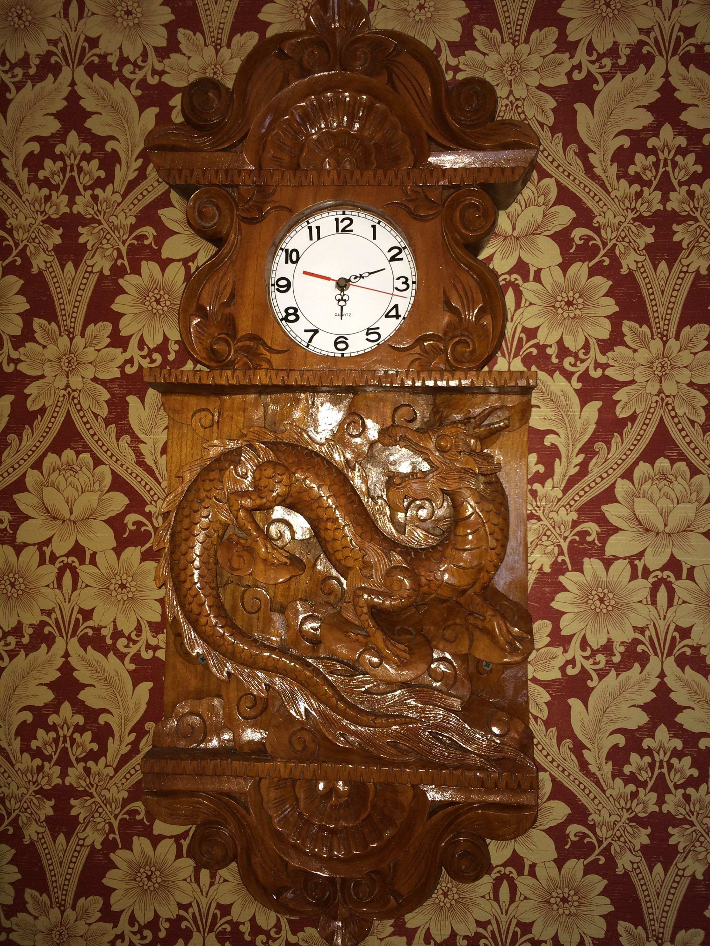 Un reloj de pared con diseño de dragón, sobre un fondo de papel tapiz floral.