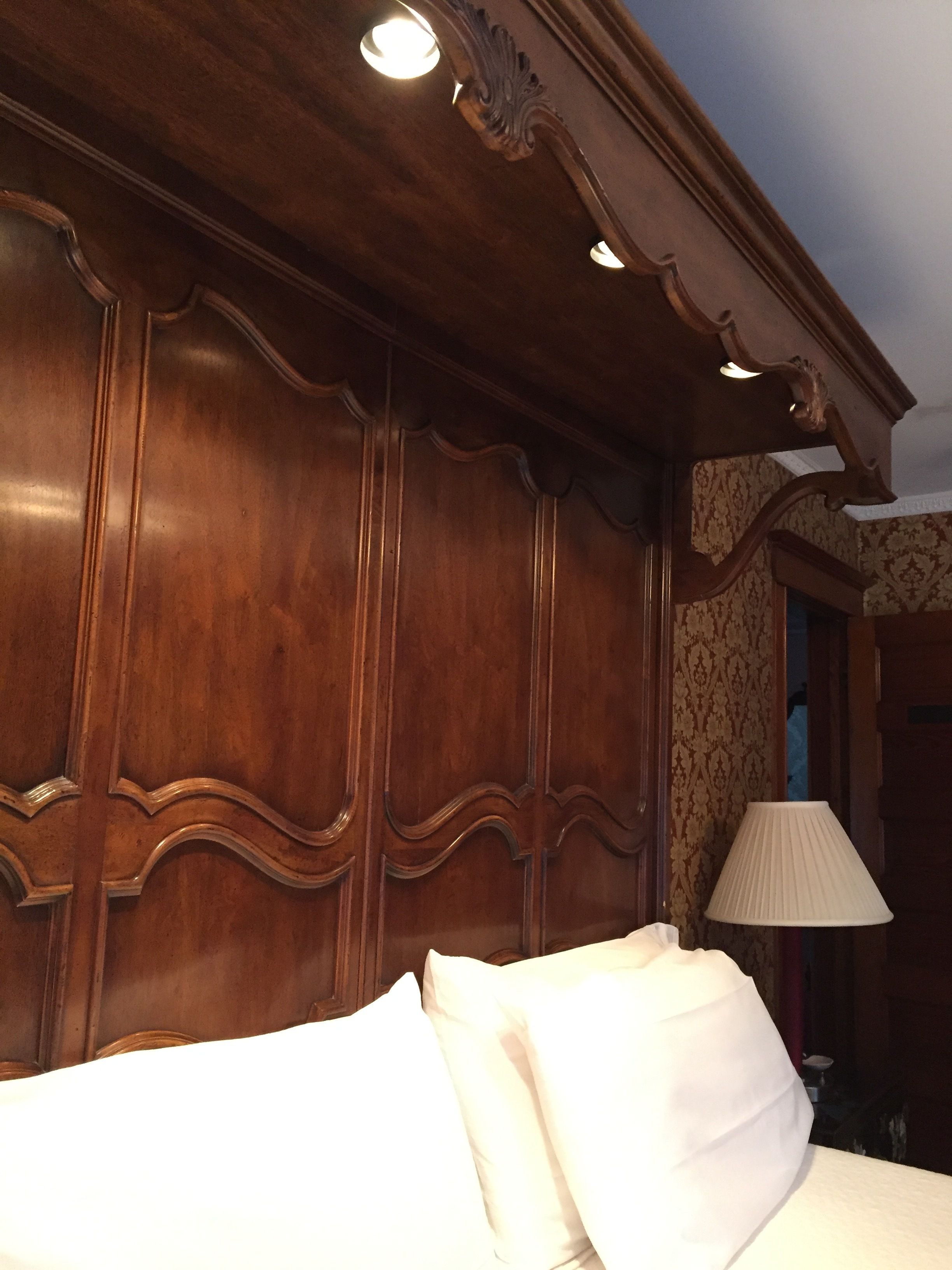 A room with a wooden headboard, a bed with white linens, and a lamp on a bedside table.