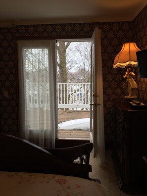 A room with a bed, a lamp, and a view of a snowy deck through a glass door.