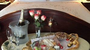 A bed with a floral bedspread, a bedside table with a bottle of champagne, glasses, and a tray of snacks. - Ginkgo Tree Inn (Mount Pleasant)