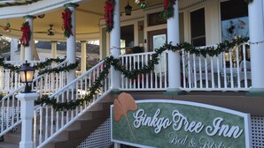 A two-story building with a porch decorated with Christmas garlands and wreaths. A sign in front reads "Ginkgo Tree Inn Bed & Bistro."