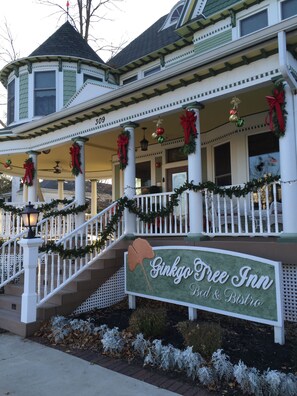 A two-story building with a porch decorated with Christmas garlands and wreaths. A sign in front reads "Ginkgo Tree Inn Bed & Bistro."