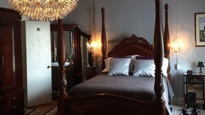 A four-poster bed with a wooden frame, a large ornate chandelier, and multiple wall sconces.