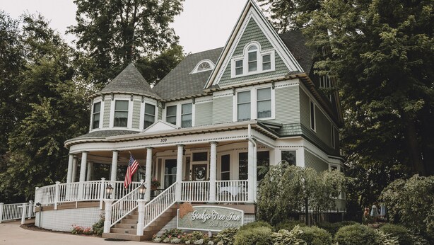 A large, historic building with a wrap-around porch, a central staircase, and a sign indicating it is a bed and breakfast. - Ginkgo Tree Inn (Mount Pleasant)