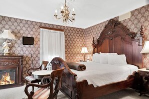 A traditional bedroom with a wooden bed, a fireplace, a chandelier, and patterned wallpaper.
