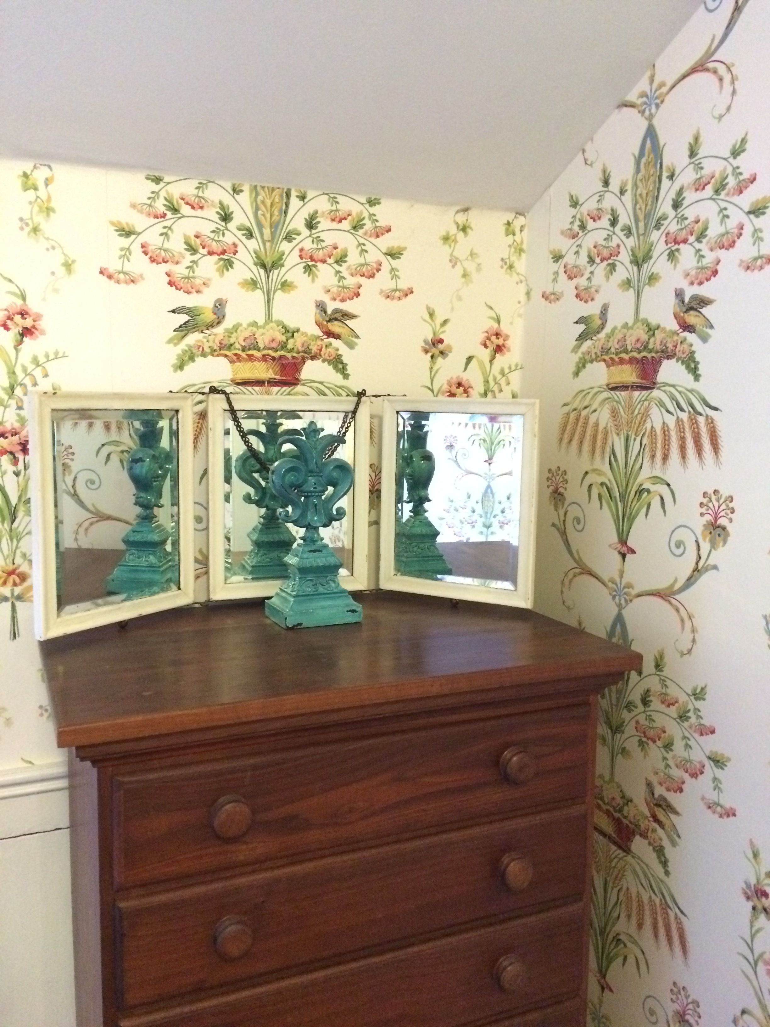 A wooden dresser with three mirrored panels and a teal decorative piece in the center.