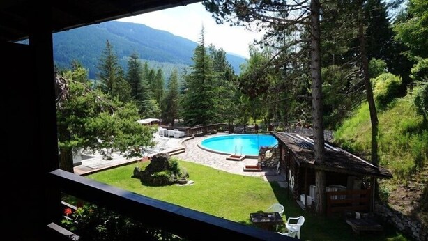 Une piscine entourée d’une terrasse en bois et d’un petit chalet, avec des montagnes en arrière-plan.