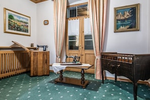 Una habitación con una máquina de coser, un escritorio de madera, un piano y una ventana con cortinas.