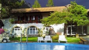 Un espace piscine avec des chaises longues, un bâtiment doté d’un toit de chaume et une vue sur les montagnes en arrière-plan.