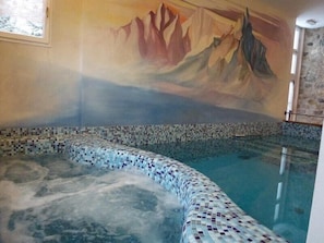 Un spa con un jacuzzi revestido de mosaicos, un mural de montañas y una pared de piedra.