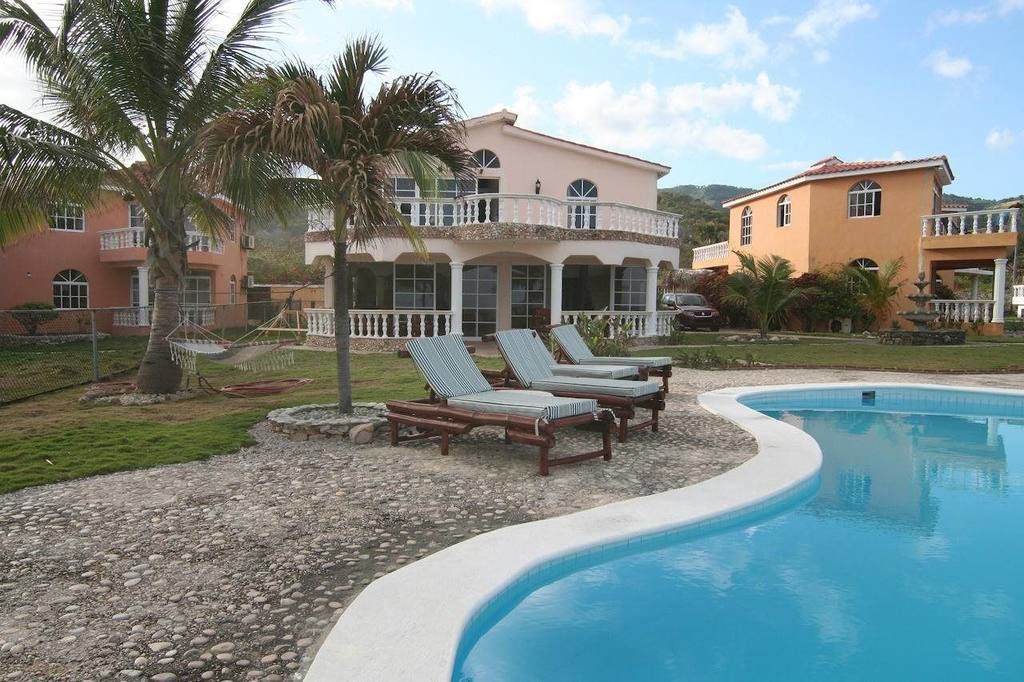 A pool area with lounge chairs, a palm tree, and a two-story building with balconies.