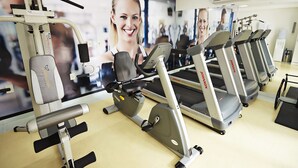 Un gimnasio con equipo de ejercicio, incluyendo cintas de correr y una máquina de pesas, además de un espejo grande que refleja el equipo y un cartel en la pared.