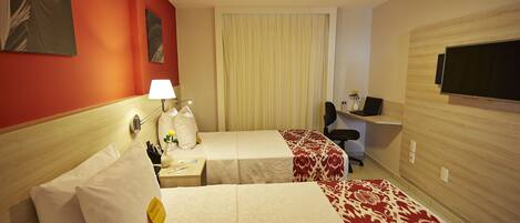 Une chambre d’hôtel avec deux lits, un bureau avec un ordinateur, une télévision et des œuvres d’art accrochées aux murs.