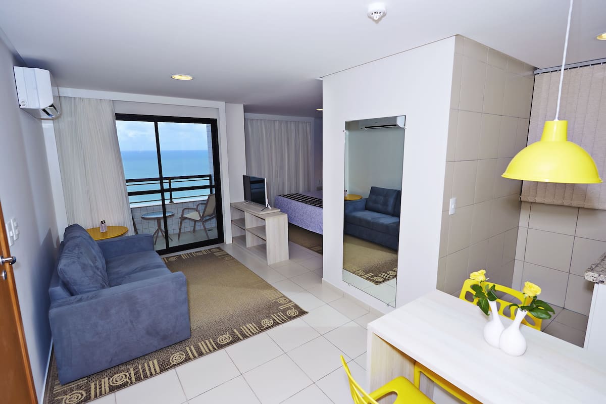 A modern hotel room with a balcony, a sofa, a desk, and a dining area.