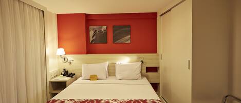 Ein Hotelzimmer mit einem Bett, einem Nachttisch, einer Lampe, einem Sessel und einer roten Akzentwand.
