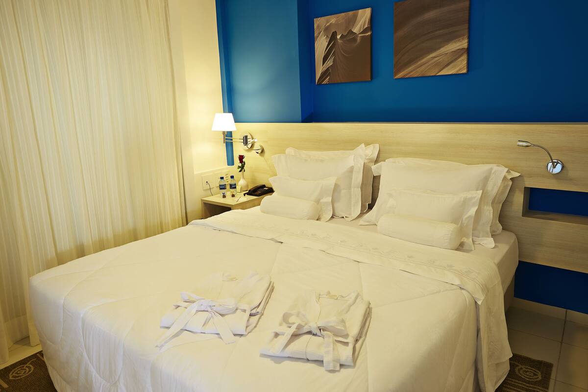 A hotel room with a large bed, two bedside tables, a lamp, and artwork on the wall.