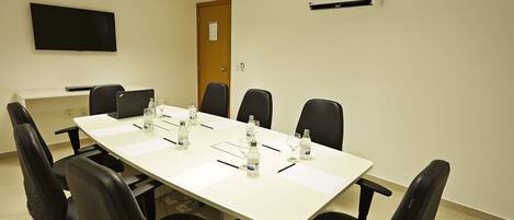 Un salón de conferencias con una mesa larga, sillas negras, un televisor de pantalla plana y un equipo de aire acondicionado.