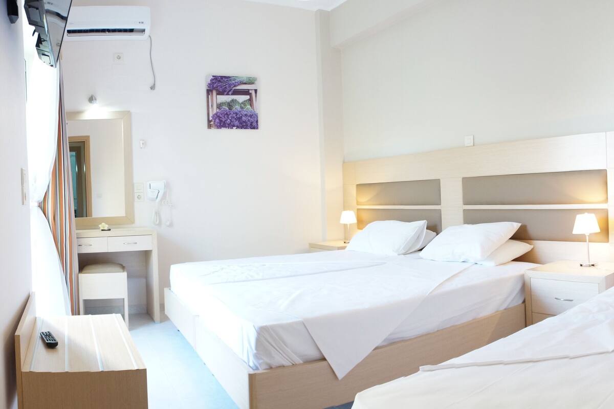 Ett hotellrum med två separata sängar, ett skrivbord med en stol, en spegel och en luftkonditioneringsanläggning.