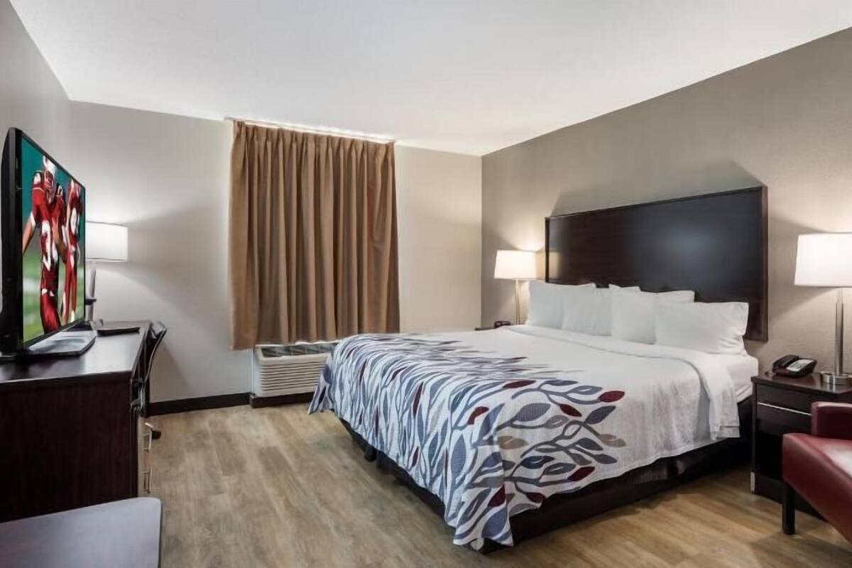 Une chambre d’hôtel avec un lit, un bureau avec une télévision, une chaise et une lampe.