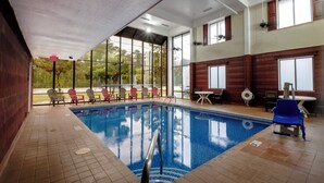 Una piscina interior con paredes de vidrio transparente, suelo de baldosas y varias sillas reclinables alrededor.