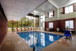 Uma piscina interior com paredes de vidro transparente, chão em azulejo e várias espreguiçadeiras ao redor.