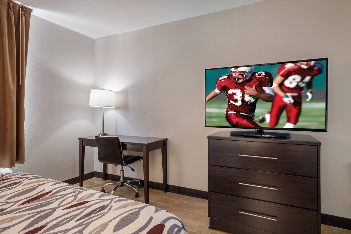 Een hotelkamer met een bed, een bureau, een stoel, een televisie en een dressoir.