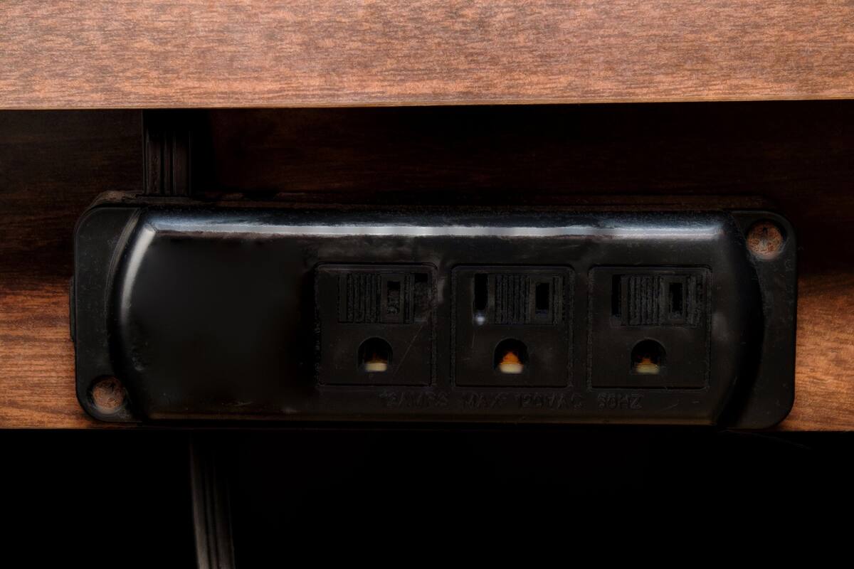 Een zwart stopcontact met drie stopcontacten, bevestigd aan een houten oppervlak.