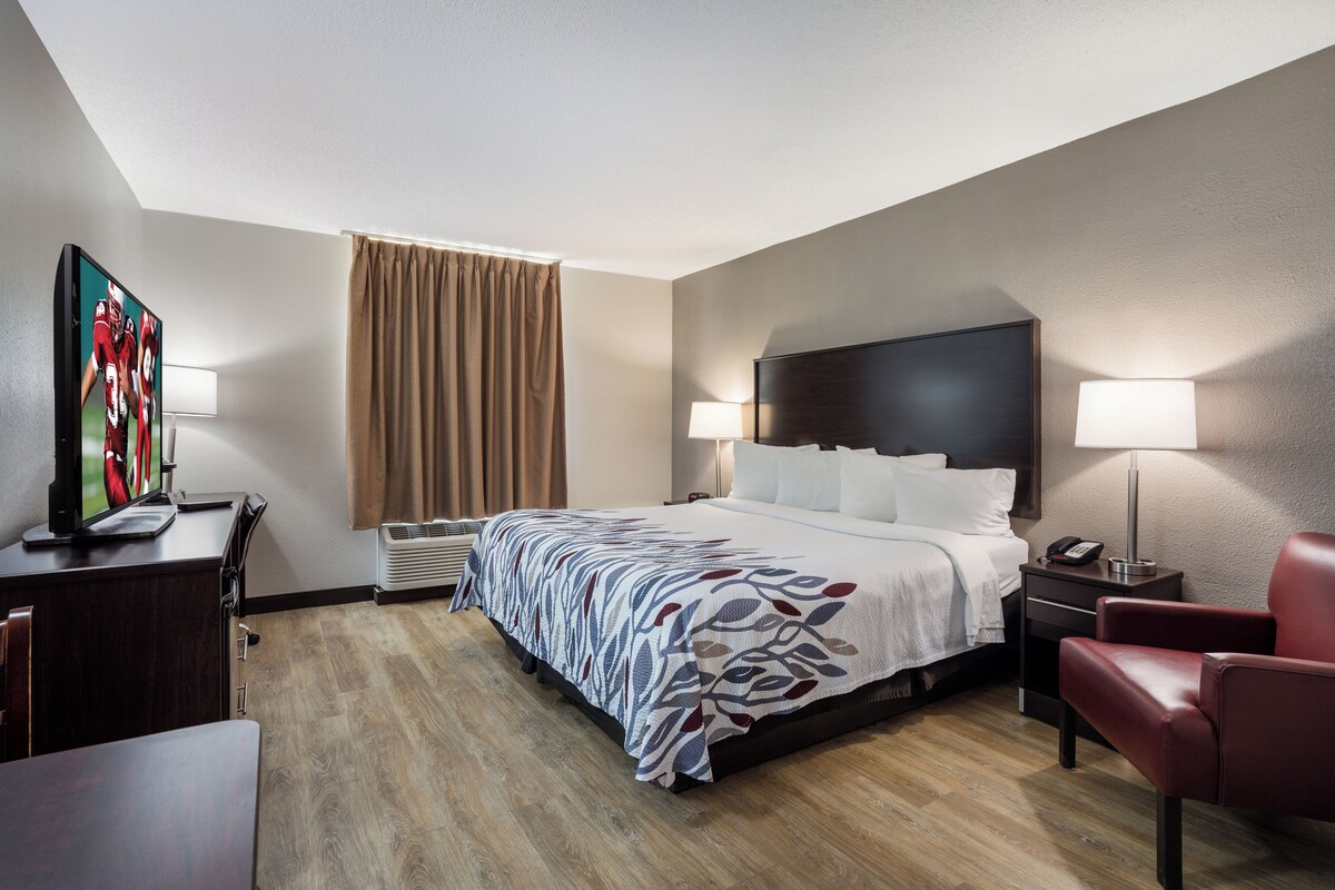 Habitación de hotel con cama, lámparas de noche, escritorio con computadora, televisor y una silla roja.