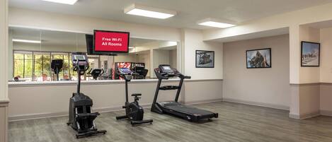 A fitness center with treadmills, stationary bikes, and a TV screen advertising free Wi-Fi.