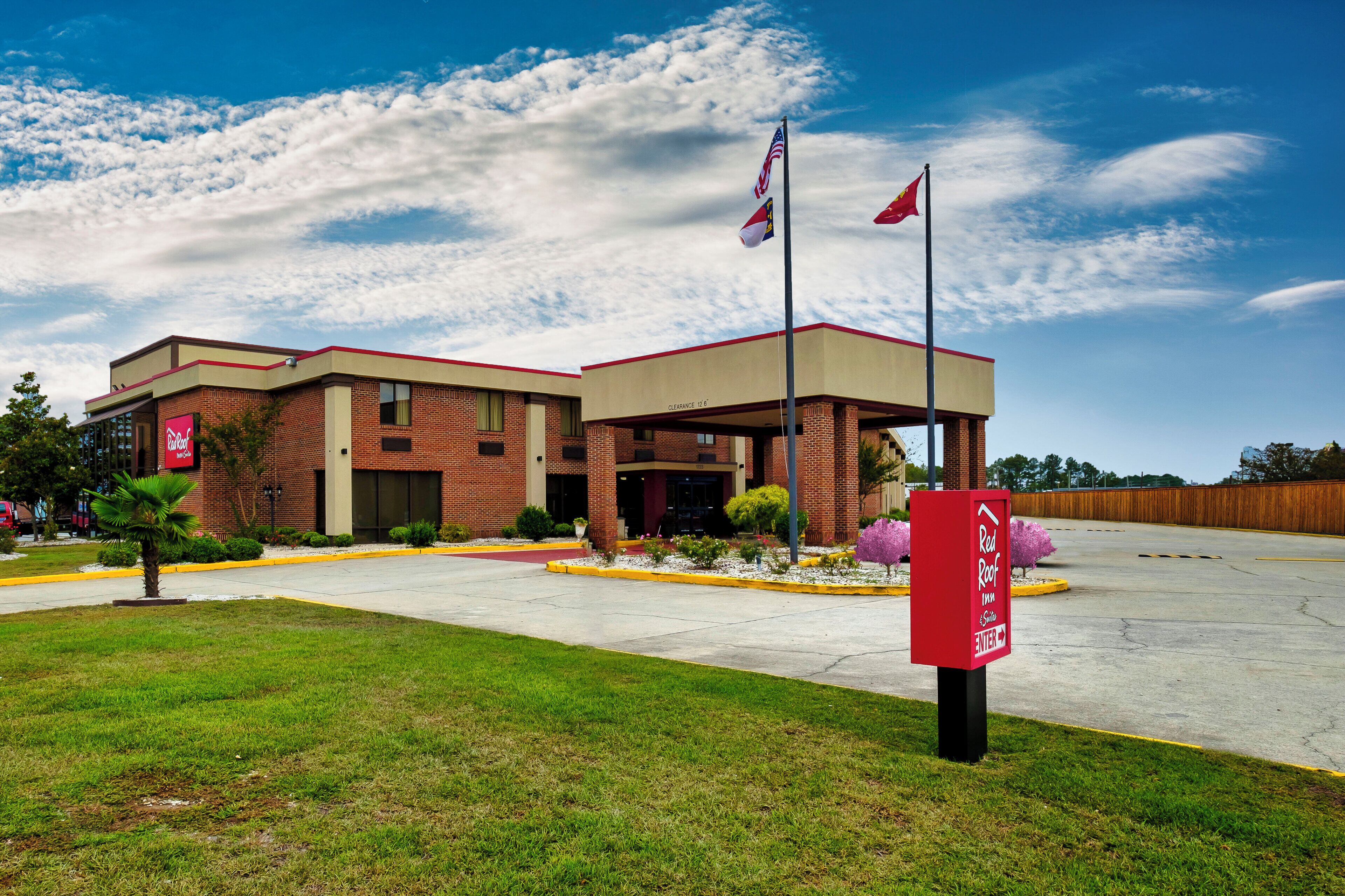 A brick building with a red roof and a covered entrance. There are flags on poles in front of the building.
