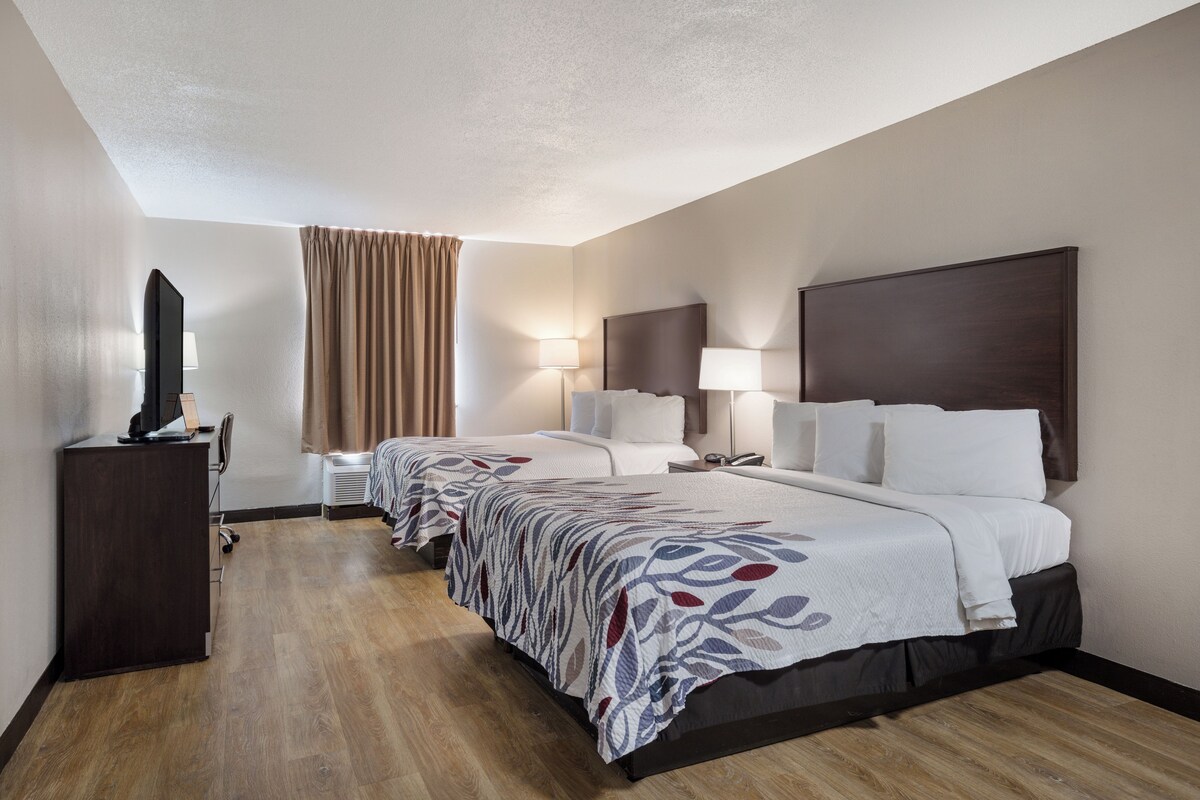 Habitación de hotel con dos camas, un escritorio, televisor y ventana con cortinas.