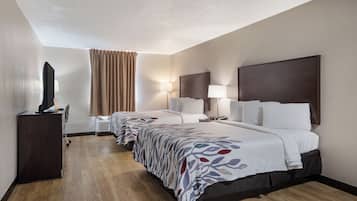 A hotel room with two beds, a TV, a desk, and a lamp.