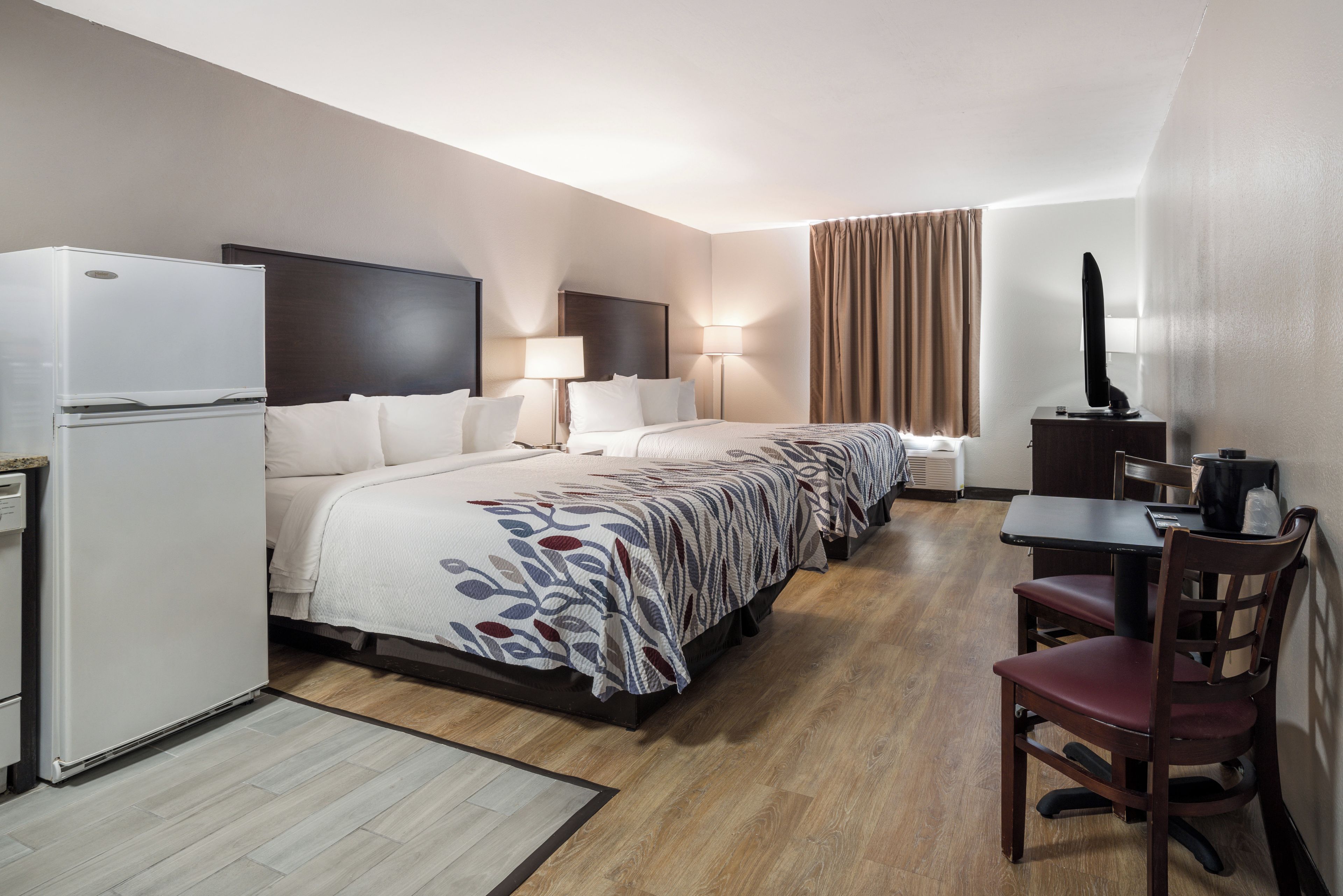 Een hotelkamer met een bed, bureau, stoel, televisie en een koelkast.