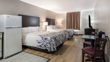 Een hotelkamer met een bed, bureau, stoel, televisie en een koelkast.