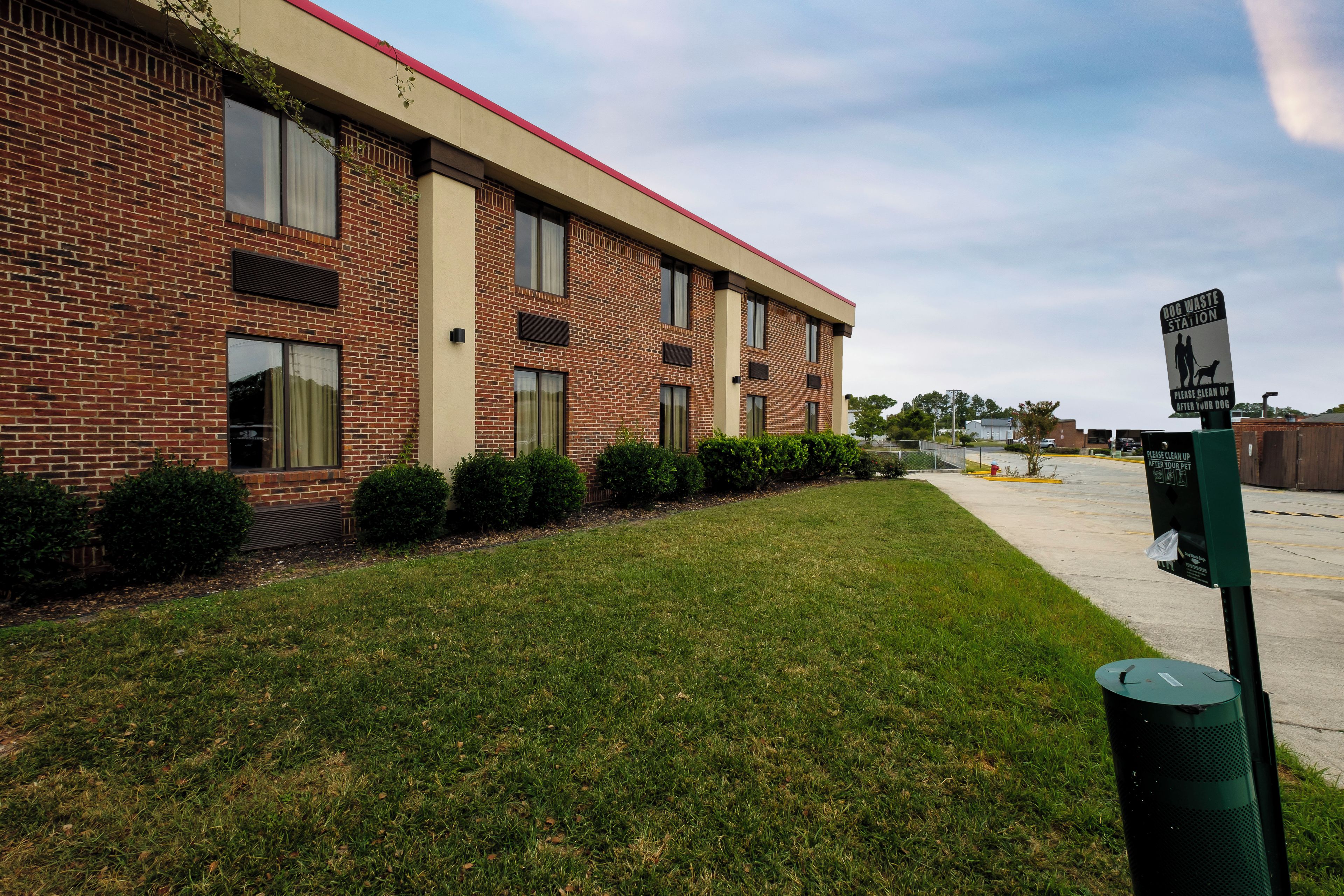 A brick building with a red roof, a grassy lawn, and a dog waste station sign.