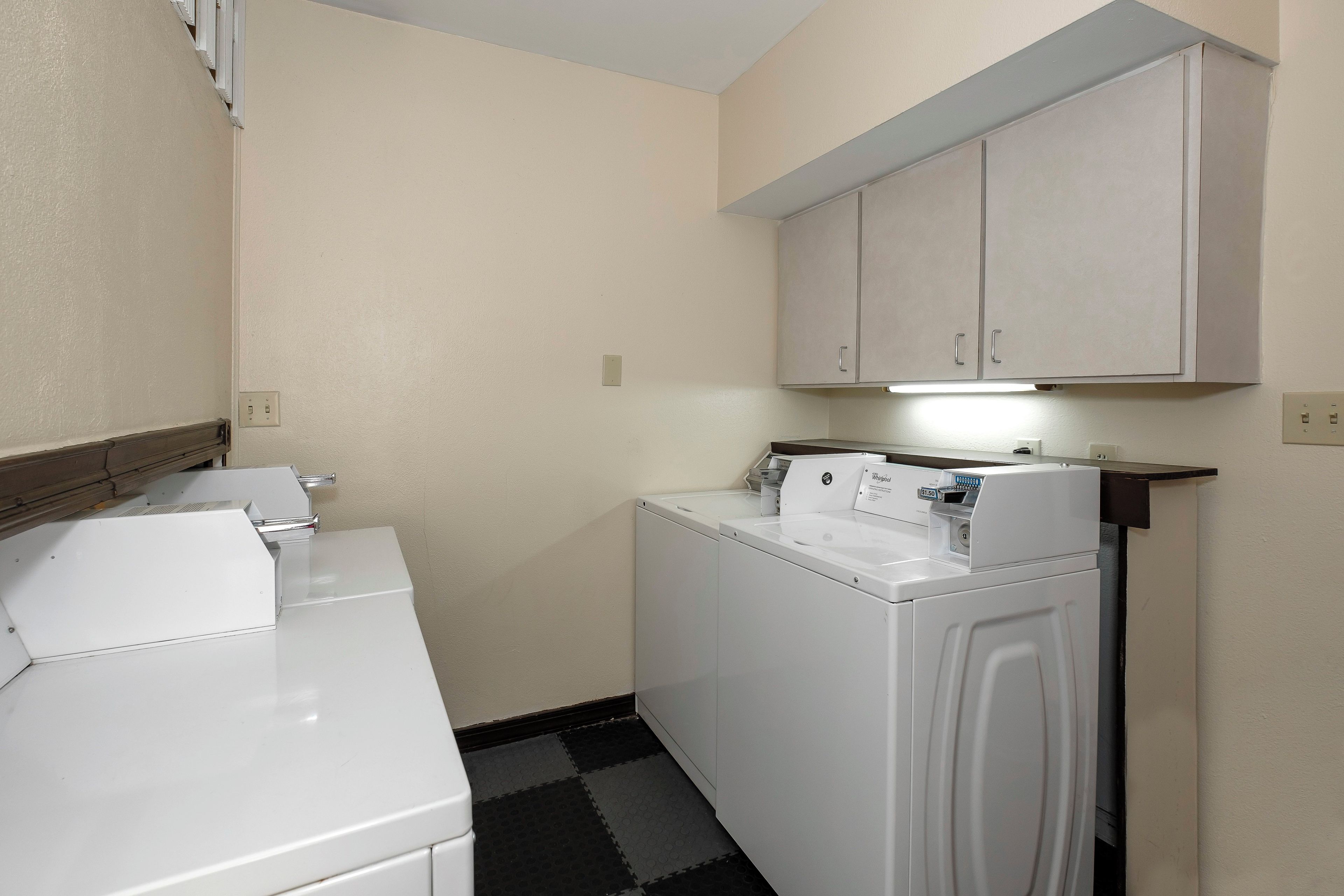 A laundry room with a washing machine and dryer, a countertop with a coffee maker, and a cabinet above the dryer.