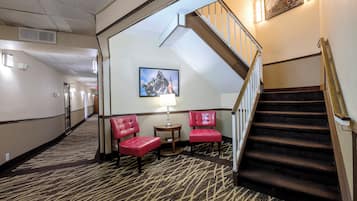 Eine Hotelhalle mit Teppichboden, einer Treppe und zwei roten Sesseln.