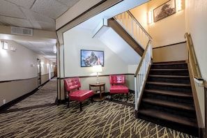 Un hall d'hôtel avec un sol recouvert de moquette, un escalier et deux fauteuils rouges.
