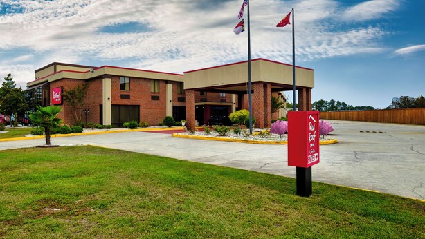 Un Red Roof Inn con un edificio de ladrillo, un estacionamiento techado y un cielo despejado.