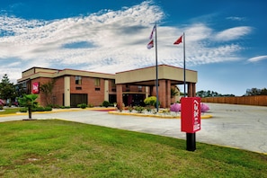 Un hôtel Red Roof Inn avec un bâtiment en briques, un espace de stationnement couvert et un ciel dégagé.
