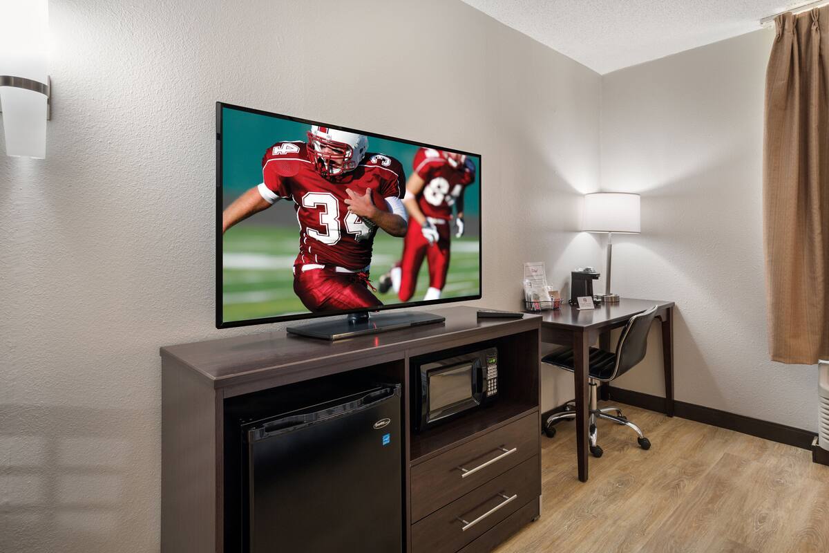 Een hotelkamer met een flatscreen televisie bevestigd aan een houten kast, een bureau met een lamp en een magnetron.