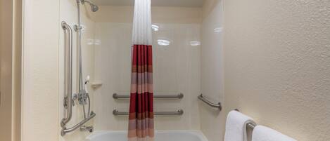 A bathroom with a bathtub, a shower with a handrail, and a towel rack.