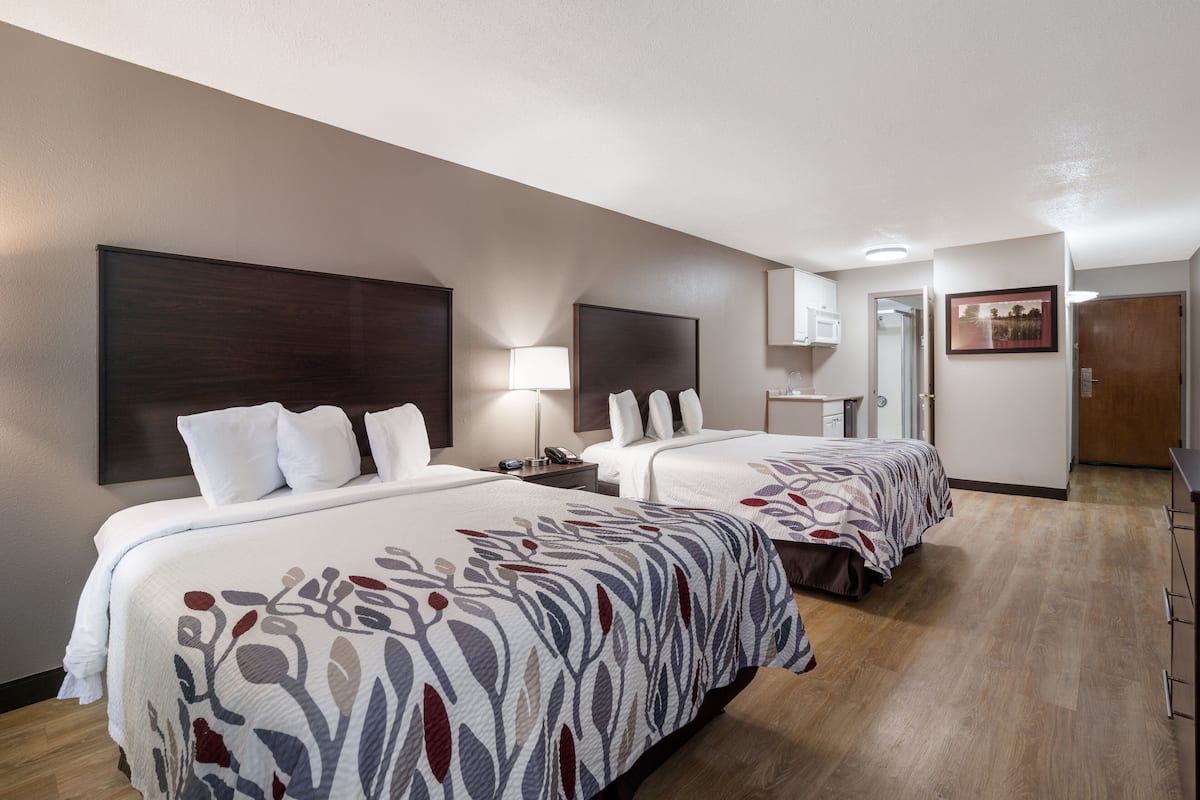 Une chambre d’hôtel avec deux lits, une table de chevet avec une lampe, un miroir et une porte donnant sur une autre pièce.