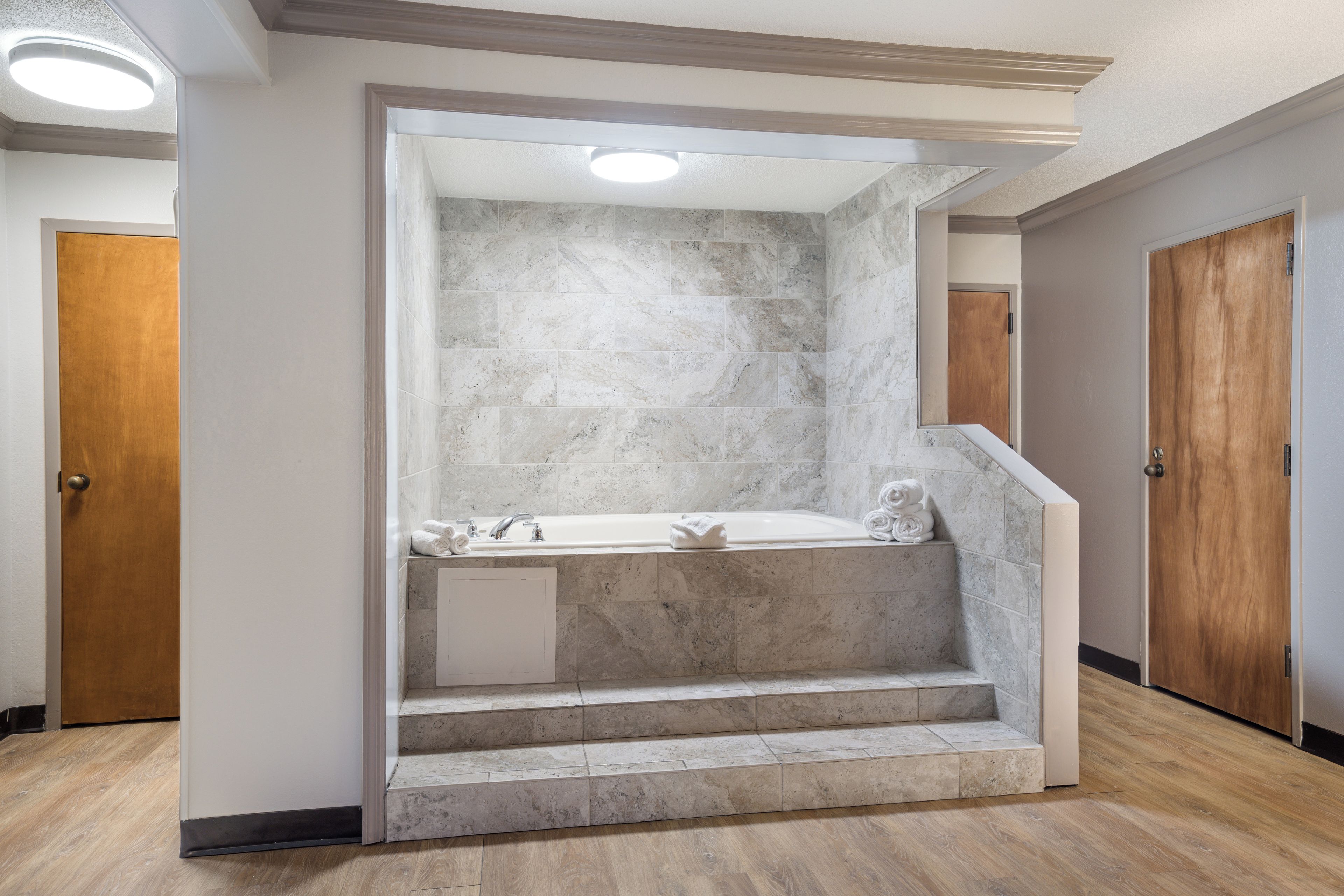 Un baño con bañera empotrada, paredes de mármol y una puerta de madera.